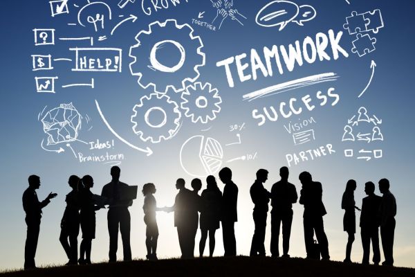 Silhouetten eines Teams vor gezeichneten Symbolen zu Teamwork, Erfolg und Kommunikation: Sinnbild für Zusammenarbeit.